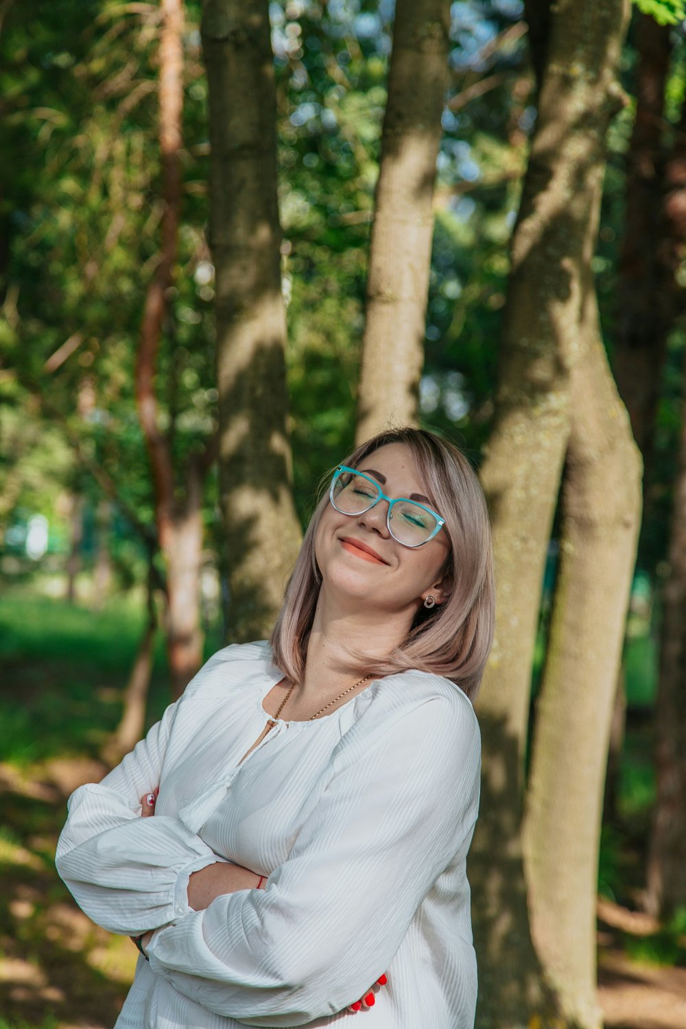 A woman with her eyes closed, content in the sunlight among the trees